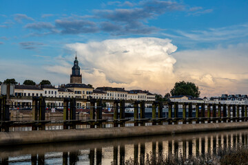 Wooden waterway passage with cityscape of Zutphen in The Netherlands behind and large cumulonimbus rain cloud rising above. Dutch climate and weather condition landscape.