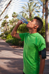 young latin athlete drinks water with eyes closed and headphones on after exercise. Sports bracelet with smart phone
