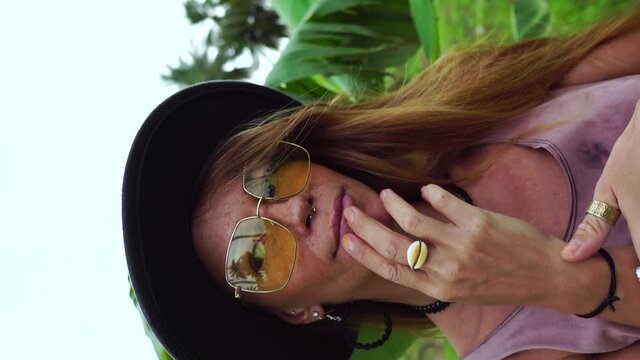 Close-up of face of a young Caucasian woman playing with her hands in a forest background. Vertical format for social media.