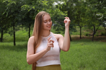 Woman applying insect repellent onto arm in park. Tick bites prevention © New Africa