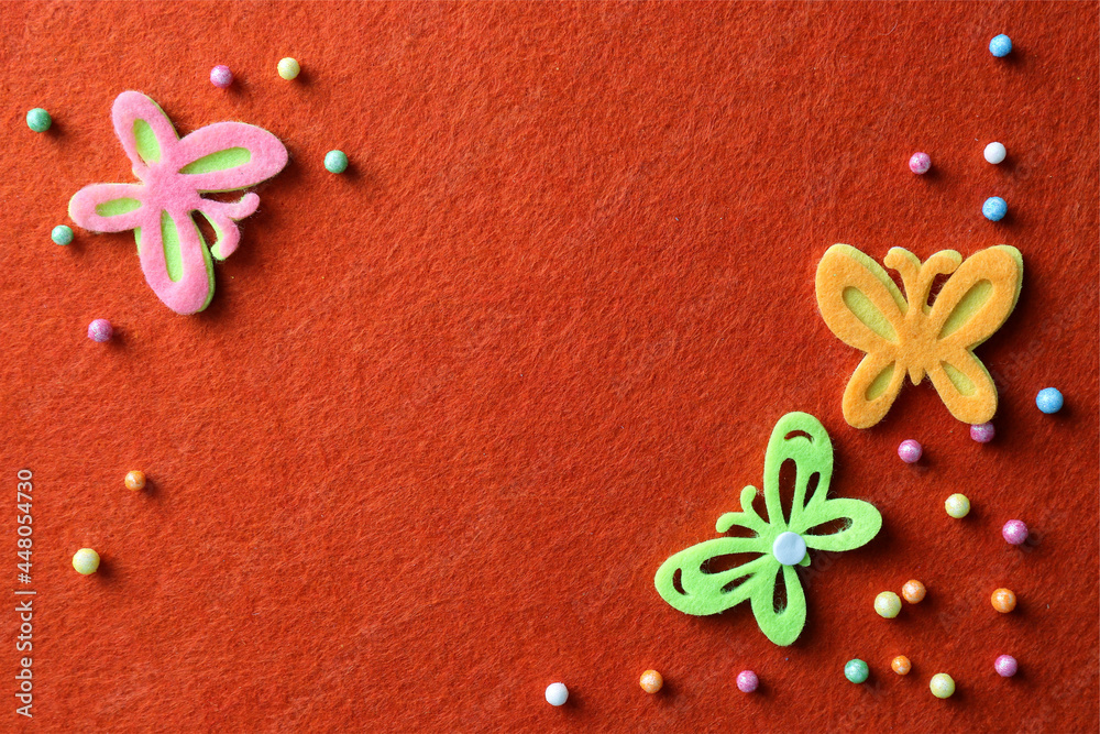 Wall mural small colorful beads and felt butterflies on red background, flat lay. space for text