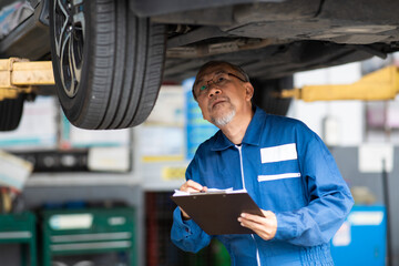 Asian senior man mechanic changing car wheel at Car maintenance and auto service garage. Elderly male worker people