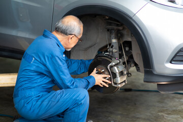 Asian senior man mechanic changing car wheel at Car maintenance and auto service garage. Elderly male worker people