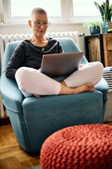 Obraz premium A dedicated senior woman is sitting in her chair at home with a laptop in her lap and finishing online business.