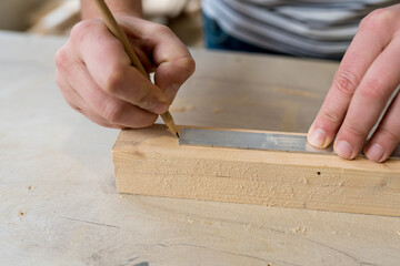 Close up of Man carpenter measuring a wooden board with a ruler with scale in workshop. Joinery work on the production and renovation of wooden furniture. Small Business Concept