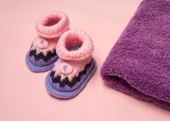Fototapeta na wymiar Knitted Baby booties and towel on pink background
