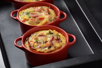 Omelette  with bacon, grated parmesan and greens in ceramic cocotte on oven tray. Tasty breakfast