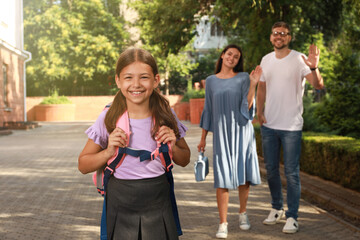 Parents waving goodbye to their daughter before school outdoors