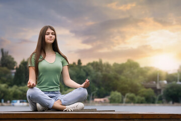 Fototapeta na wymiar Teenage girl meditating near river. Space for text