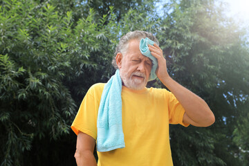 Senior man with towel suffering from heat stroke outdoors