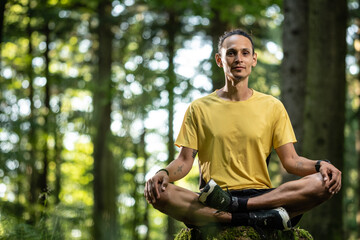 Junger Mann mit dunkler Haut sitzt im Wald und meditiert auf Baumstamm