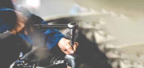 Caucasian male mechanic repairs car in garage. Car maintenance and auto service garage concept. Close up mechanical hand and spanner.