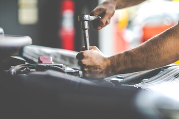 Caucasian male mechanic repairs car in garage. Car maintenance and auto service garage concept. Closeup hand and spanner.