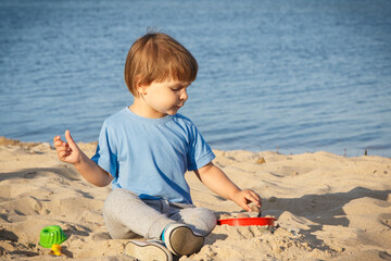 Baby boy playing with sand on summer beach. Vacation time and child development concept