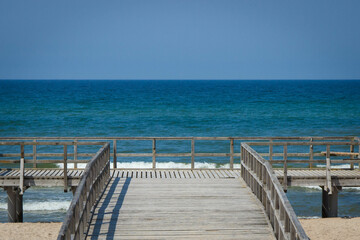 Fototapeta na wymiar Wooden empty jetty or pier and beach by sunny sea. Travel, tourism and summer time