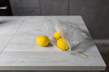 Three lemons in a plastic transparent bag are on a wooden table in a beige kitchen interior. Making lemonade