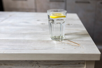 Transparent glass tables with a slice of lemon are on a wooden table in a beige kitchen interior. Empty space