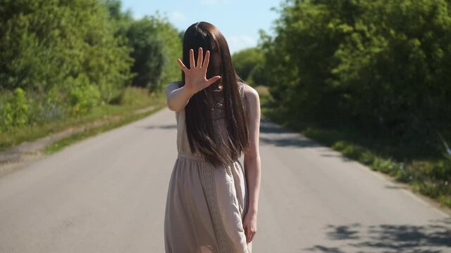 Portrait of scary ghost woman in an old dress with hair covering her face, shows her stop palm at the camera. Horror on the road creepy day for travelers.