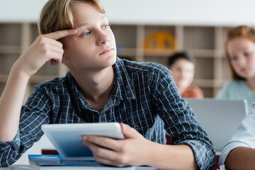 Pensive schoolboy holding digital tablet in classroom