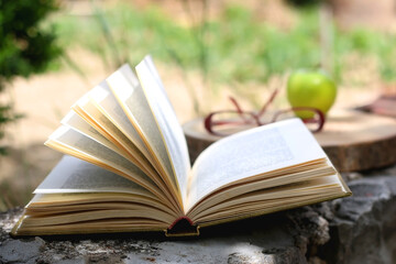 Red reading glasses, green apple and open book. Selective focus.