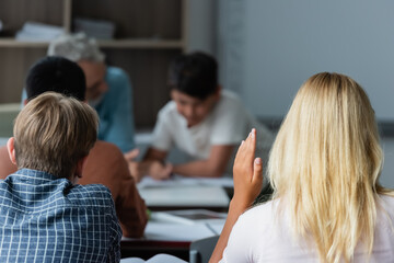 Schoolgirl raising hand near classmates in classroom