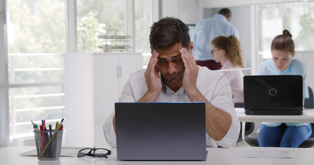 Exhausted indian male employee having headache sitting at desk