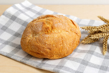 white bread on a napkin with a checkered drawing and wheat on a wooden table