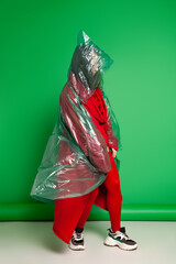 Calm female wearing transparent plastic raincoat and red clothes standing on green background in studio