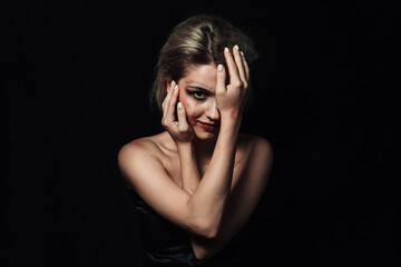 Portrait of a girl on a black background. A girl with smeared makeup covered half of her face with her hands.