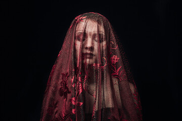 The girl's face is covered with a red veil on a black background. Dark image of a girl