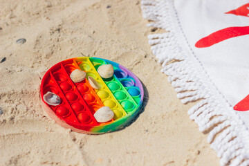 New popular silicone colorful antistress toy for baby on the beach in the sand near the bedspread. Simple dimple.