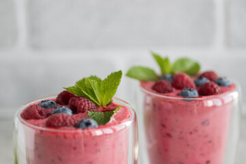 Berry smoothies in glass cups and blueberries and raspberries on a light background.