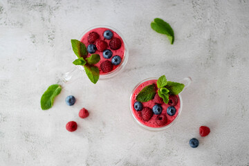 Berry smoothies in glass cups and blueberries and raspberries on a light background. Top view.