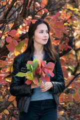 Beautiful young woman in forest. Portrait of brunette girl with autumn leaves in her hands. Vertical frame