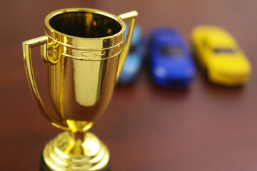Racing competition concept, golden trophy cup and blurred car models.