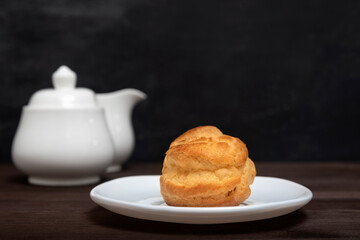Homemade profiterole, puff, popover, eclair on white plate on teapot background. Close up dessert