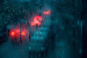 Raindrops on a window with blurred bokeh traffic lights on a background - moody, gloomy, concept of...