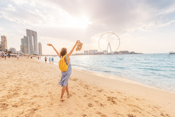 Happy female tourist walks barefoot on a sandy beach in the JBR area of Dubai and admires the...