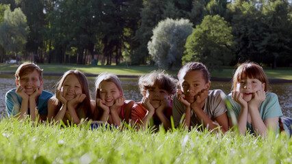 Portrait of diverse children lying on grass in park and smiling at camera - Powered by Adobe