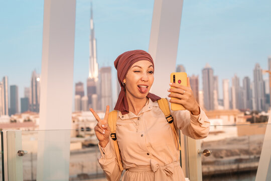 Funny woman wearing headdress takes selfie photos on her mobile phone in Dubai against the backdrop of the financial center and skyscrapers