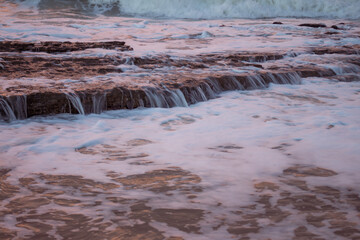 Rocks on the beach during sunset. Waves and sea foam in the form of a cloud.