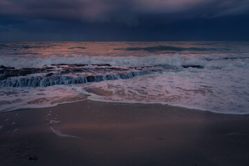 Rocks on the beach during sunset. Waves and sea foam in the form of a cloud.
