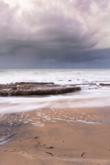 Rocks on the beach during sunset. Waves and sea foam in the form of a cloud.