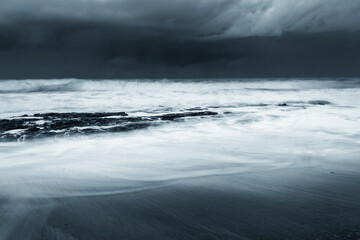 Rocks on the beach during sunset. Waves and sea foam in the form of a cloud.