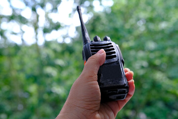 close-up female hand holds black gadget, portable radio station, receiving-transmitting device designed for operational communication on natural background, concept of modern technologies in forest