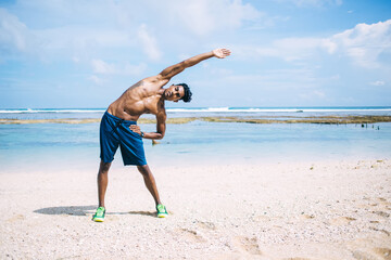 Focused ethnic athlete exercising and bending to side at seaside