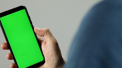 A man's hand holds a green screen smartphone.  