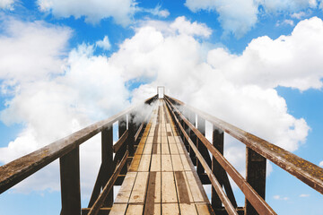 Wooden bridge going into the clouds. Clouds in the sky with a bridge. Unknown, success or fear concept