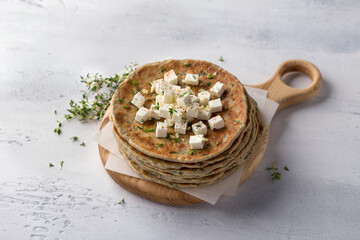 Obraz na płótnie Canvas Homemade yeast-free gluten-free buckwheat flat bread with feta cheese, thyme and spices on wooden board, light blue textured background. Healthy food concept