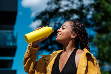 Attractive young woman drinking from a yellow bottle.